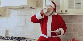 圣诞老人坐在厨房家具上，吃着加牛奶的饼干