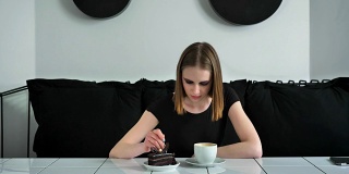 年轻漂亮的女人浓妆艳抹地坐在沙发上吃着蛋糕，黑白的咖啡馆背景