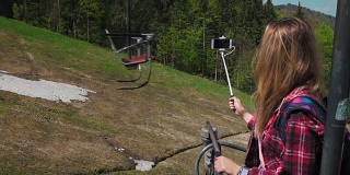 年轻女子在登山缆车上，用智能手机和自拍杆自拍。瑞士森林的背景。慢动作