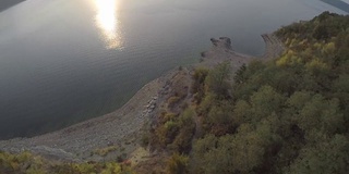 日落时，在宽阔的河边的森林上空进行了一次奇妙的飞行。夏季日落时松树林的鸟瞰图。aeril视图