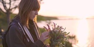美丽的年轻女子拿着一束野花在日落的海岸上