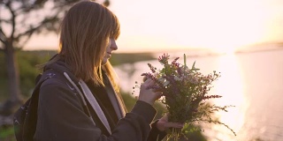 美丽的年轻女子拿着一束野花在日落的海岸上