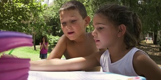 孩子们在夏令营外面做作业，在公园的树下，坐在桌子上，躺在地上慢动作