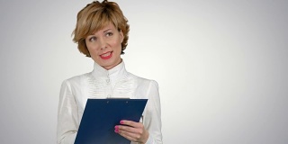 年轻漂亮的商务女性穿着西装，面带微笑，心情愉快，用平板电脑工作，在白色背景上写信息