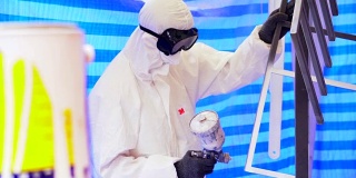 慢镜头:一个戴着防护面具、穿着工作服的成年人正在粉刷家具