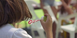 年轻的小女孩使用吹泡器在绿色的田野夏令营外面的慢镜头