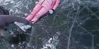 女孩在冰上又飞又滚。年轻的夫妇有乐趣在冬季散步的背景冰冻结的湖。情侣们躺在有裂缝的透明冰面上，嬉戏、亲吻、拥抱。从以上观点。