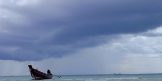 在浅海中，长尾船在海滩附近摆动。背景是泰国的风暴云