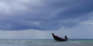 在浅海中，长尾船在海滩附近摆动。背景是泰国的风暴云