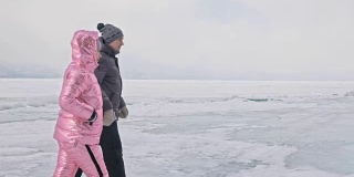 年轻的夫妇有乐趣在冬季散步的背景冰冻结的湖。情侣们走在冰上，手牵着手，亲吻和拥抱。蜜月。爱情故事。