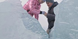 年轻的夫妇有乐趣在冬季散步的背景冰冻结的湖。爱情故事。情人躲在冰后面亲吻。快乐的年轻人在冰雪覆盖的冰面上漫步。蜜月。