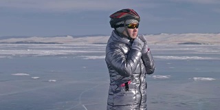 女人穿着运动器材。这个女孩穿着银色的羽绒服，背着自行车背包，戴着头盔。结冰的贝加尔湖的冰。自行车的轮胎上覆盖着特殊的尖钉。