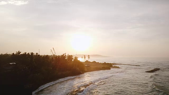 Drone flying forward above beautiful sunset beach, white ocean waves reaching coast line with ongoing construction site