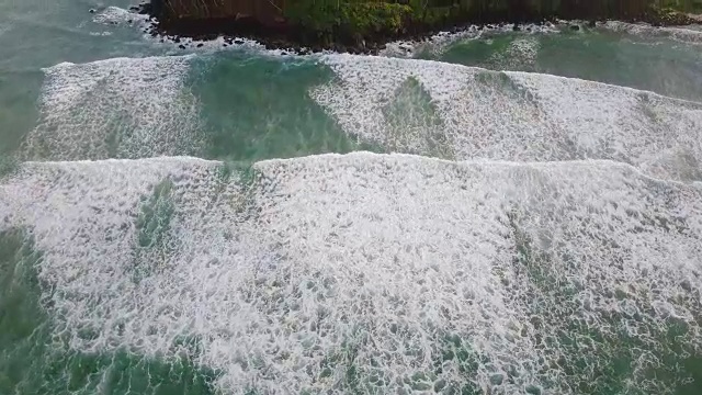 无人机飞过碧波汹涌的大海，然后到达海岸边的热带岛屿上的棕榈树