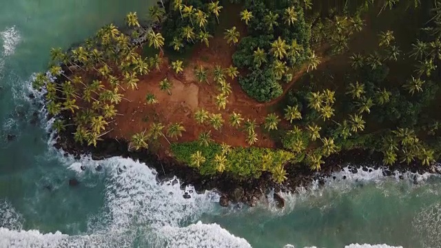 史诗般的鸟瞰图，白色的海浪到达海岸与热带岛屿上的棕榈树和度假屋