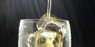 将饮料倒入加冰的玻璃杯中，并滴入水滴。黑色背景。近距离