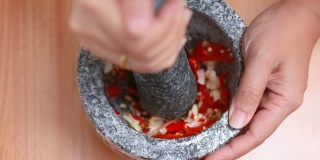 俯视女子用手捶打红辣鲜辣椒和大蒜，用臼石准备混合香草调味料，烹饪泰国菜前用暖调加工