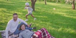 父母躺在草地上-孩子们有乐趣和跑步背景在公园