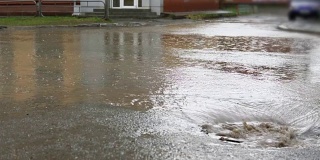 雨水落在路上，流过下水道。汽车在被水淹没的道路上行驶。