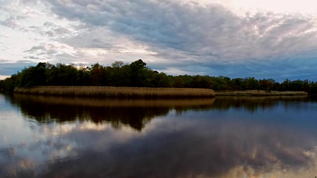 日落时，风暴云在湖面上移动。彩色天空的蓝色，黄色和橙色的日出在全高清高清视频