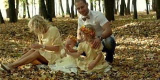 妈妈，爸爸和孩子们在公园里的空地上玩耍，在枫叶的飘落中