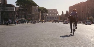 在阳光明媚的日子里，年轻的潮人骑着自行车走向罗马市中心的斗牛场