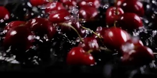 成熟的樱桃浆果落入水中，背景是黑色的。慢动作