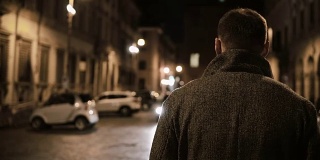 年轻时尚的男人走在深夜穿过黑暗的街道，在晚上独自走