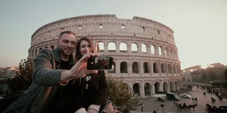 一对年轻幸福的情侣在用智能手机自拍。意大利罗马圆形大剧场附近的帅哥美女
