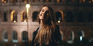 晚上，年轻美丽的女子站在意大利罗马圆形大剧场附近，微笑着回望着镜头