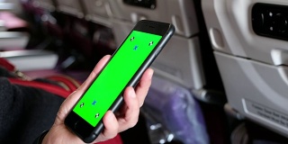 近距离女人的手看在绿色屏幕的手机应用程序在飞机座位