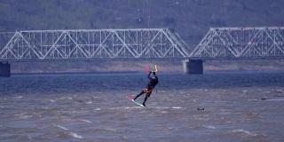慢动作:一名男子的风筝滑板越过一条大河的水面。水花四溅向不同的方向。阳光明媚的春天。