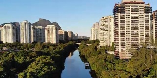 夏日的一天，无人机在巴拉达蒂茹卡(Barra da Tijuca)的马拉潘迪运河(Marapendi canal)上空拍摄，一艘船在河上缓缓行驶。两侧是高耸的住宅楼，绿草如茵