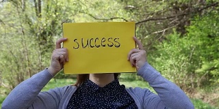 一个年轻的女人拿着一张黄色的纸，上面写着成功