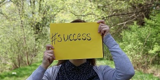 一个年轻的女人拿着一张黄色的纸，上面写着成功