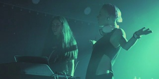 夜店里，两个年轻漂亮的女DJ在调音台播放音乐。在一群不认识的人的背景下。慢动作