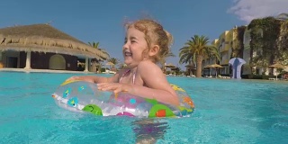 在炎热的夏日里，快乐的小女孩在室外游泳池里玩五彩缤纷的充气圈。孩子们在热带度假胜地玩耍。孩子们学游泳。家庭海滩度假。