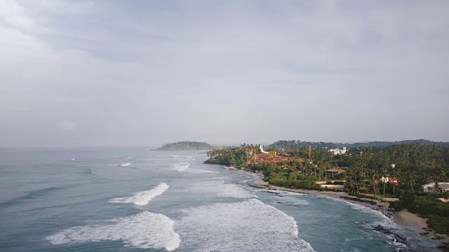 无人机在空中拍摄的田园诗般的泡沫海浪到达壮观的热带度假村海岸的建筑