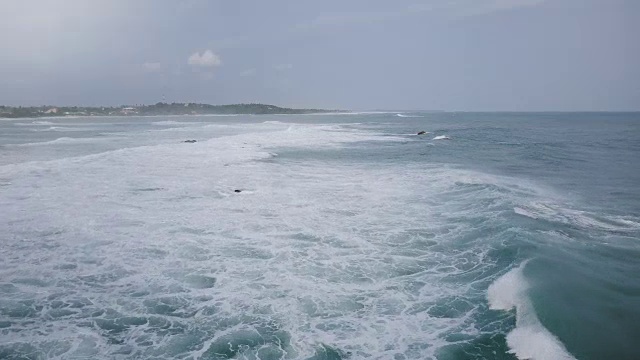 难以置信的鸟瞰图，巨大的海浪冲刷礁岩，到达异国情调的热带海岸下多云的天空