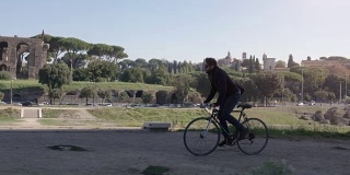 年轻的潮人骑自行车在道路上circo massimo公园废墟在罗马城市中心在阳光明媚的日子慢镜头车