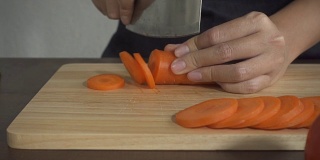 慢镜头-女人做健康的食物和切胡萝卜在厨房的砧板上。