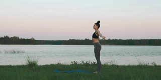 年轻女孩穿着运动服做瑜伽早上在湖与copyspace