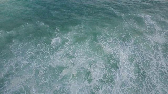 无人机向后飞行在一个令人惊讶的蓝色和薄荷绿色的天然海泡纹理的海浪后面升起