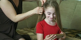 女人的手为她的小女儿做发型。一位妇女正在为她的女儿编头发。