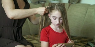 女人的手为她的小女儿做发型。一位妇女正在为她的女儿编头发。