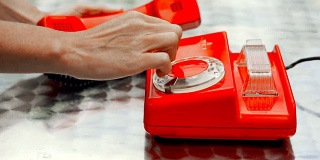 红色古董旋转电话在桌子上，侧面观看。女性的一只手拨通电话，另一只手拿着听筒。