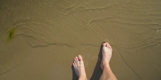 一个男人的腿走在浅水上，走在沙滩上