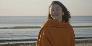 一个美丽的年轻女孩的近距离肖像在海滩上微笑，而风吹她的头发