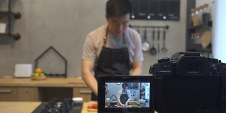 年轻的亚洲人在厨房里给摄像机录像。微笑的亚洲人工作的食物博主概念与水果和蔬菜在厨房。
