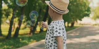 戴着帽子的小孩在接泡泡。夏天的一天，小男孩在外面玩耍
